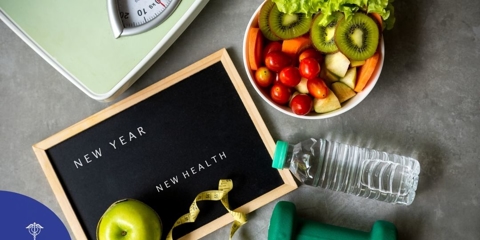 Board that reads "New Year, New Health" with an apple on it, a weight, water bottle, salad, and scale are also on the counter.