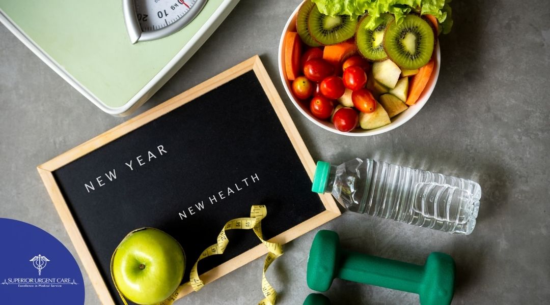 Board that reads "New Year, New Health" with an apple on it, a weight, water bottle, salad, and scale are also on the counter.