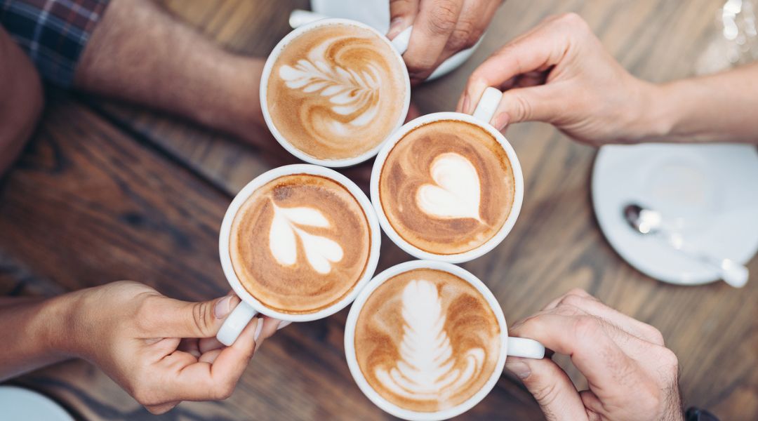 Photo of 4 individuals holding cups of coffee with latte art.